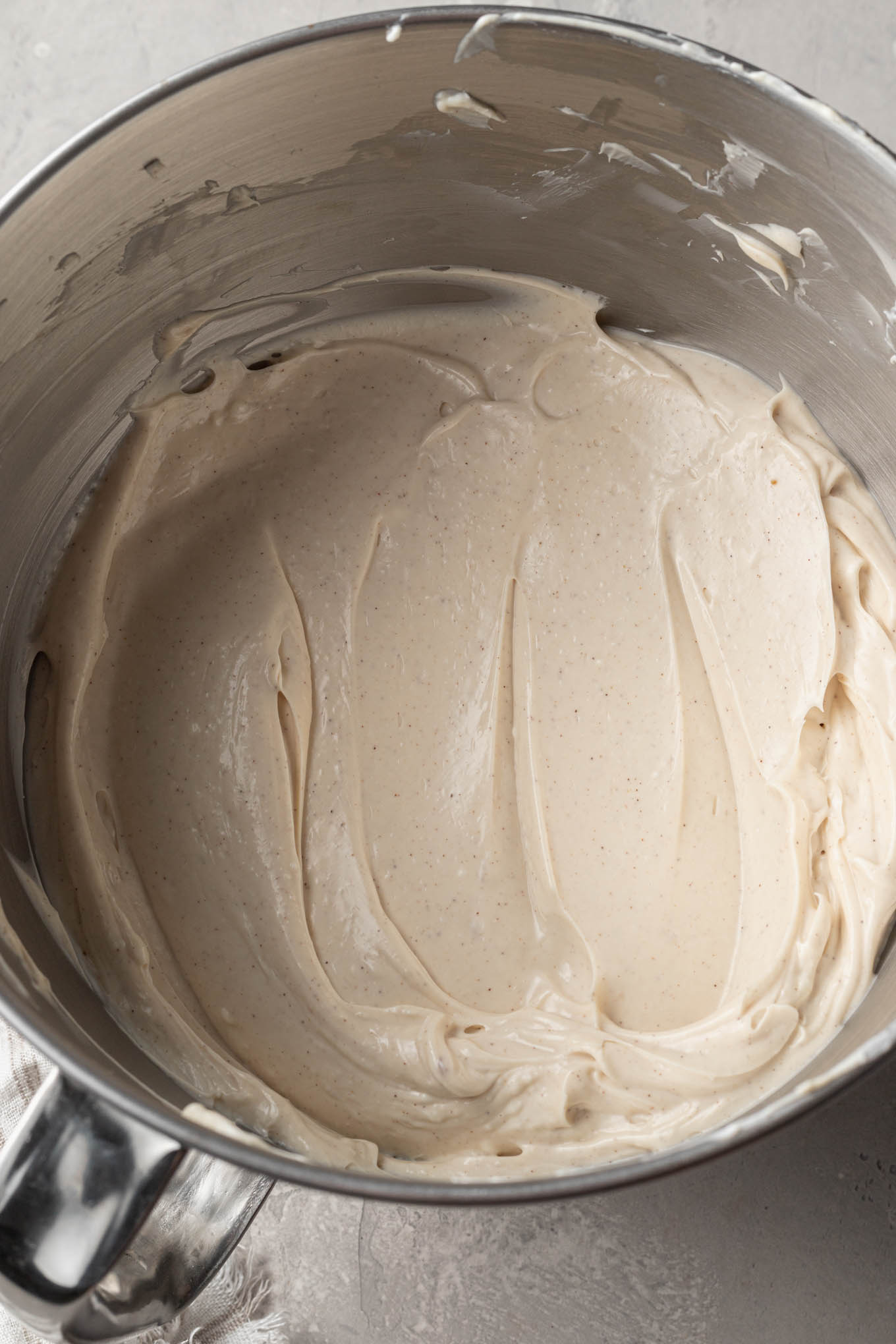 An overhead view of cheesecake filling in the bowl of a stand mixer, with a paddle attachment. 