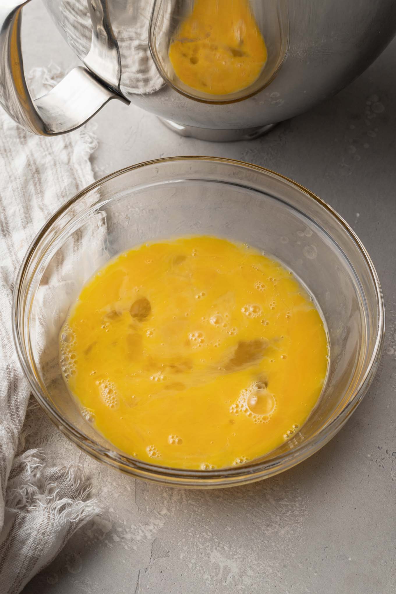 An overhead view of beaten eggs in a glass mixing bowl. 