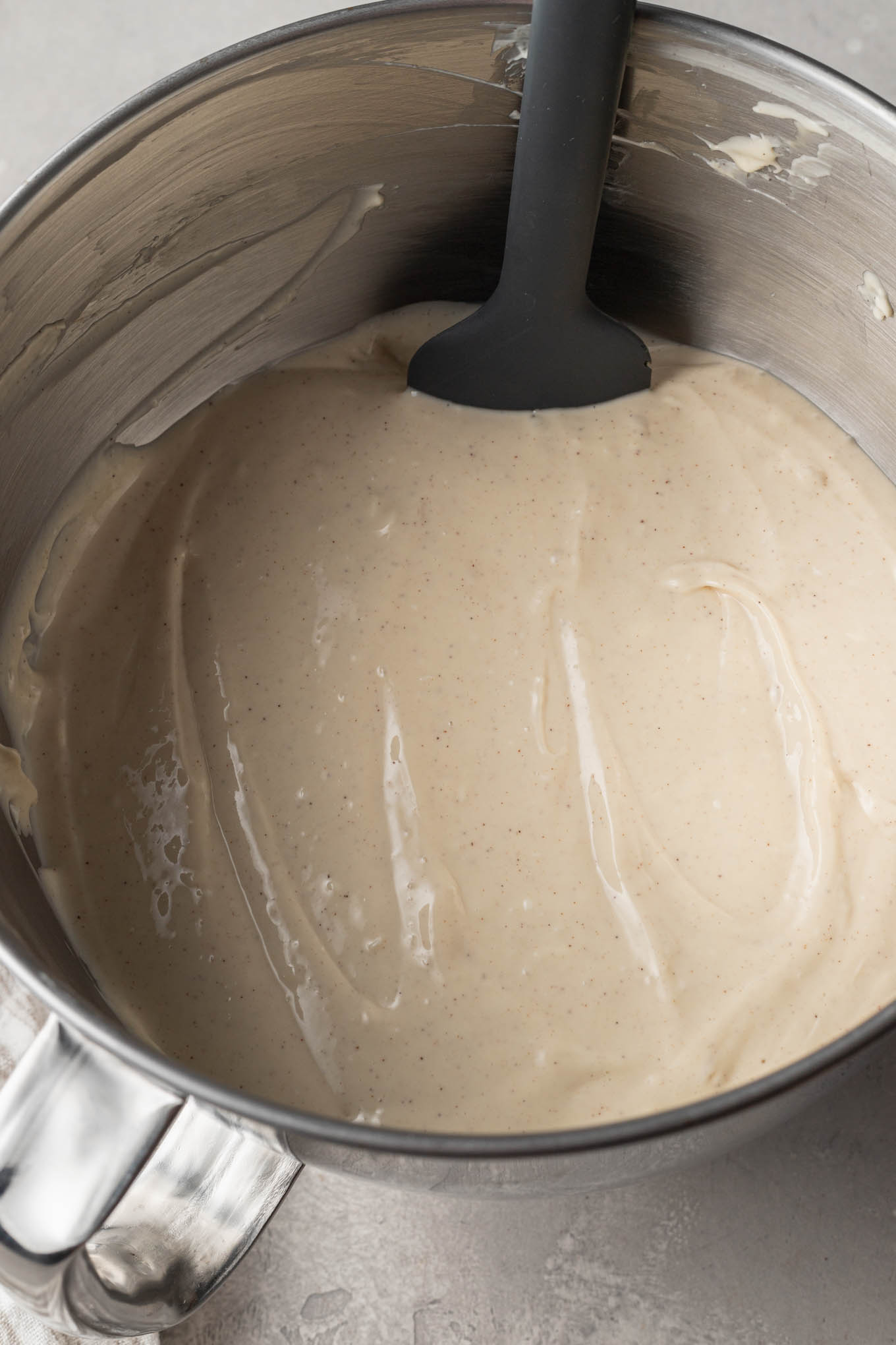 An overhead view of cheesecake filling in the bowl of a stand mixer, with a rubber spatula. 