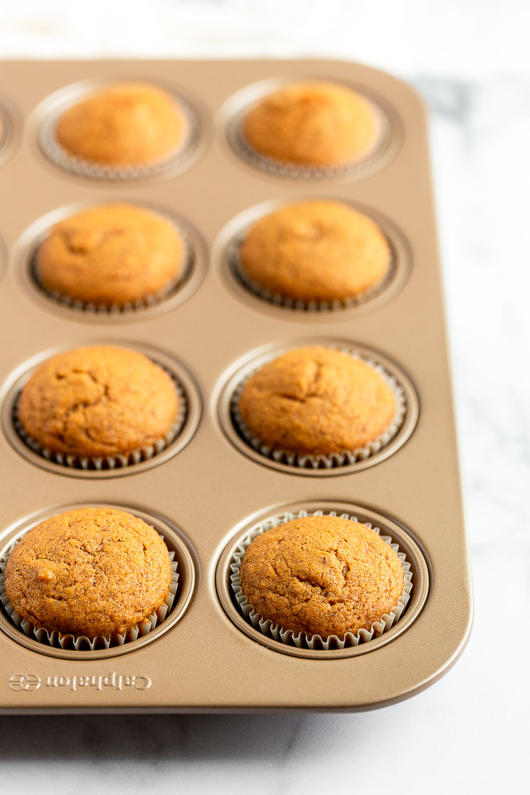 Un molde para muffins relleno de cupcakes de calabaza recién salidos del horno.