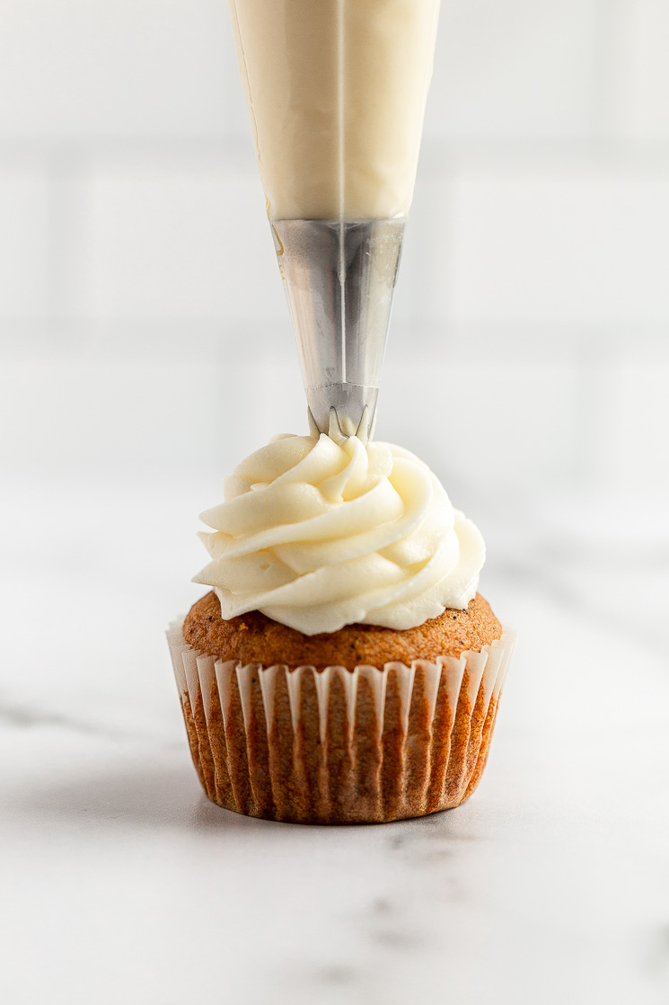 Un solo cupcake de calabaza cubierto con glaseado de queso crema usando una manga pastelera.