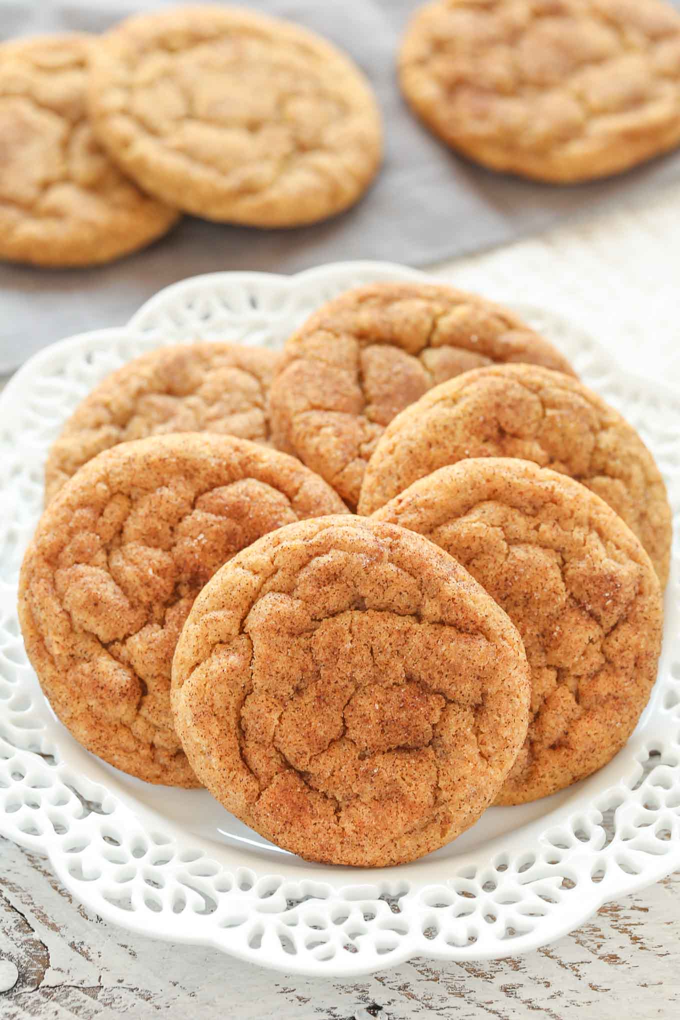 Un plato blanco con seis galletas masticables de calabaza. Tres galletas más descansan al fondo.