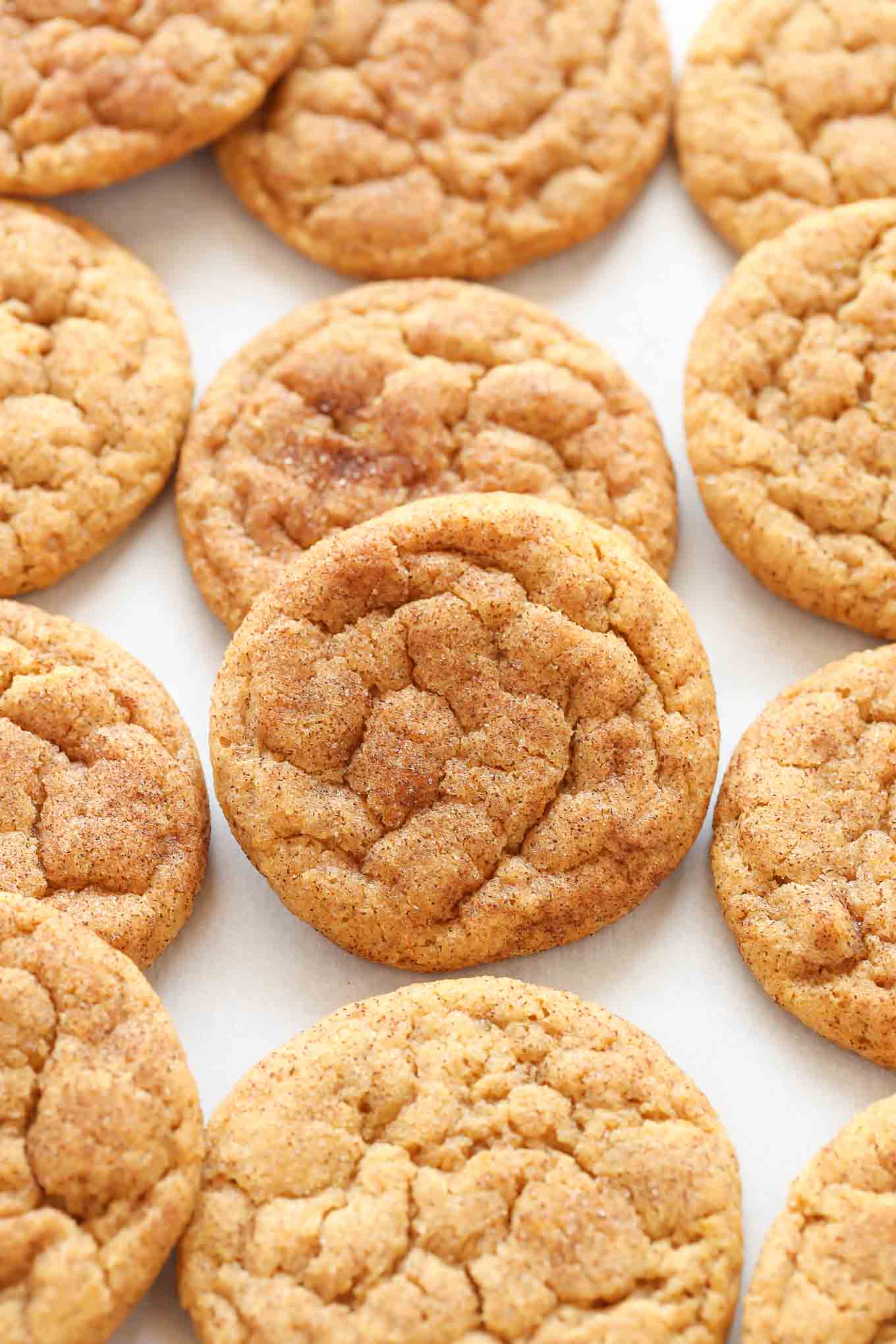 Varios snickerdoodles de calabaza sobre un trozo de papel pergamino blanco.