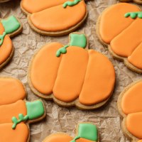 Varias galletas heladas de azúcar y calabaza sobre un trozo de papel pergamino.