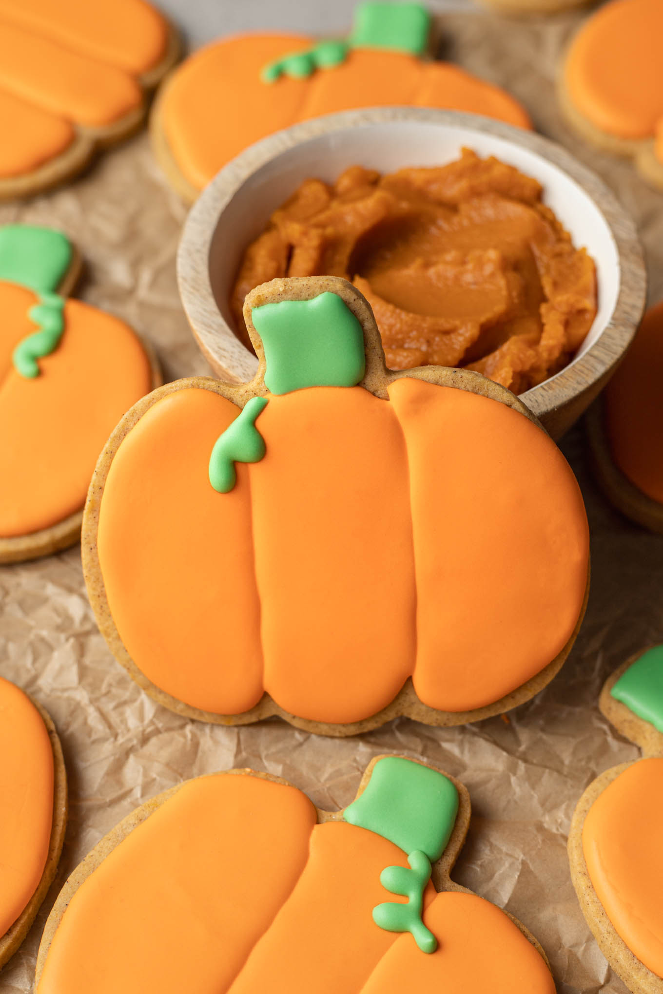 Una galleta de azúcar con forma de calabaza apoyada sobre un plato pequeño de puré de calabaza. 