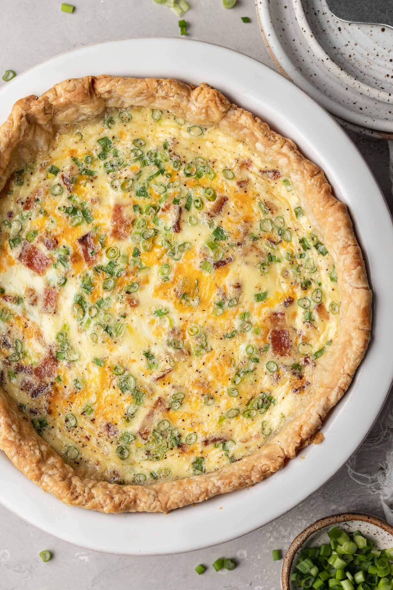 Una vista aérea de una quiche de tocino y queso al horno en un plato de pastel blanco. 