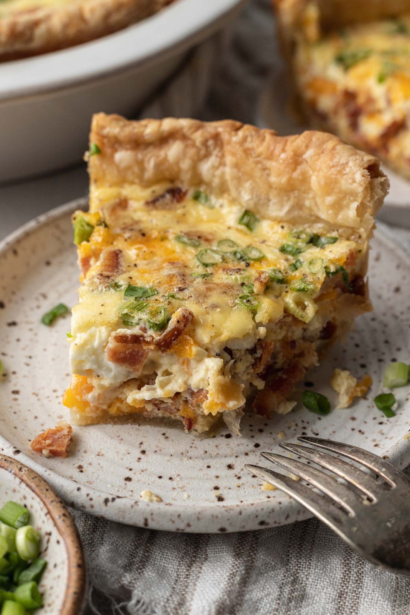 Una rebanada de quiche a la que le falta un bocado, en un plato moteado. 