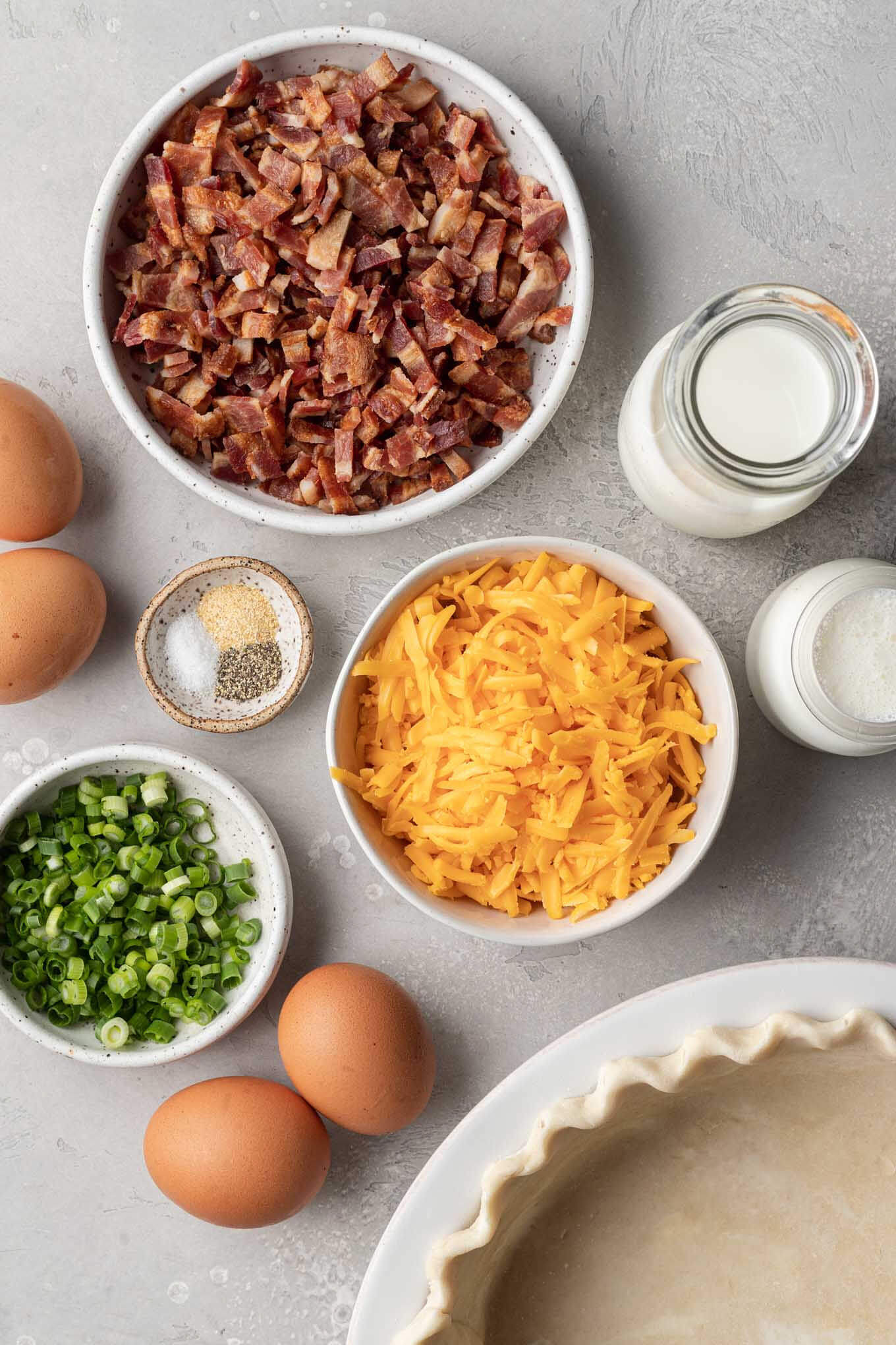 Una vista aérea de los ingredientes necesarios para hacer quiche de tocino y queso cheddar. 