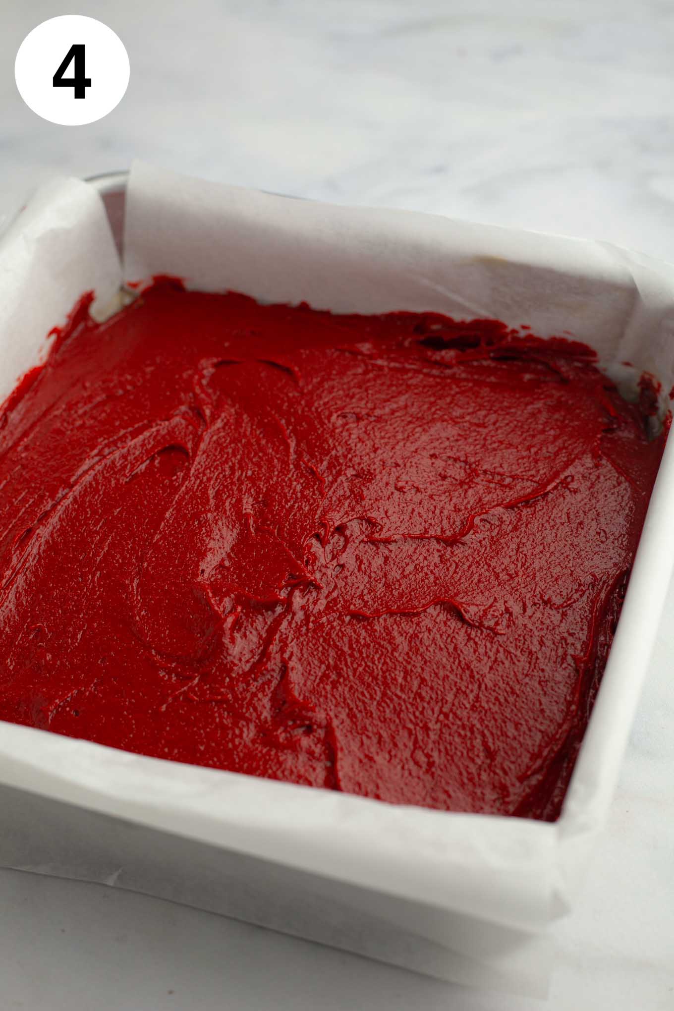 La masa de brownie de terciopelo rojo se alisó en un molde para hornear forrado con papel pergamino.