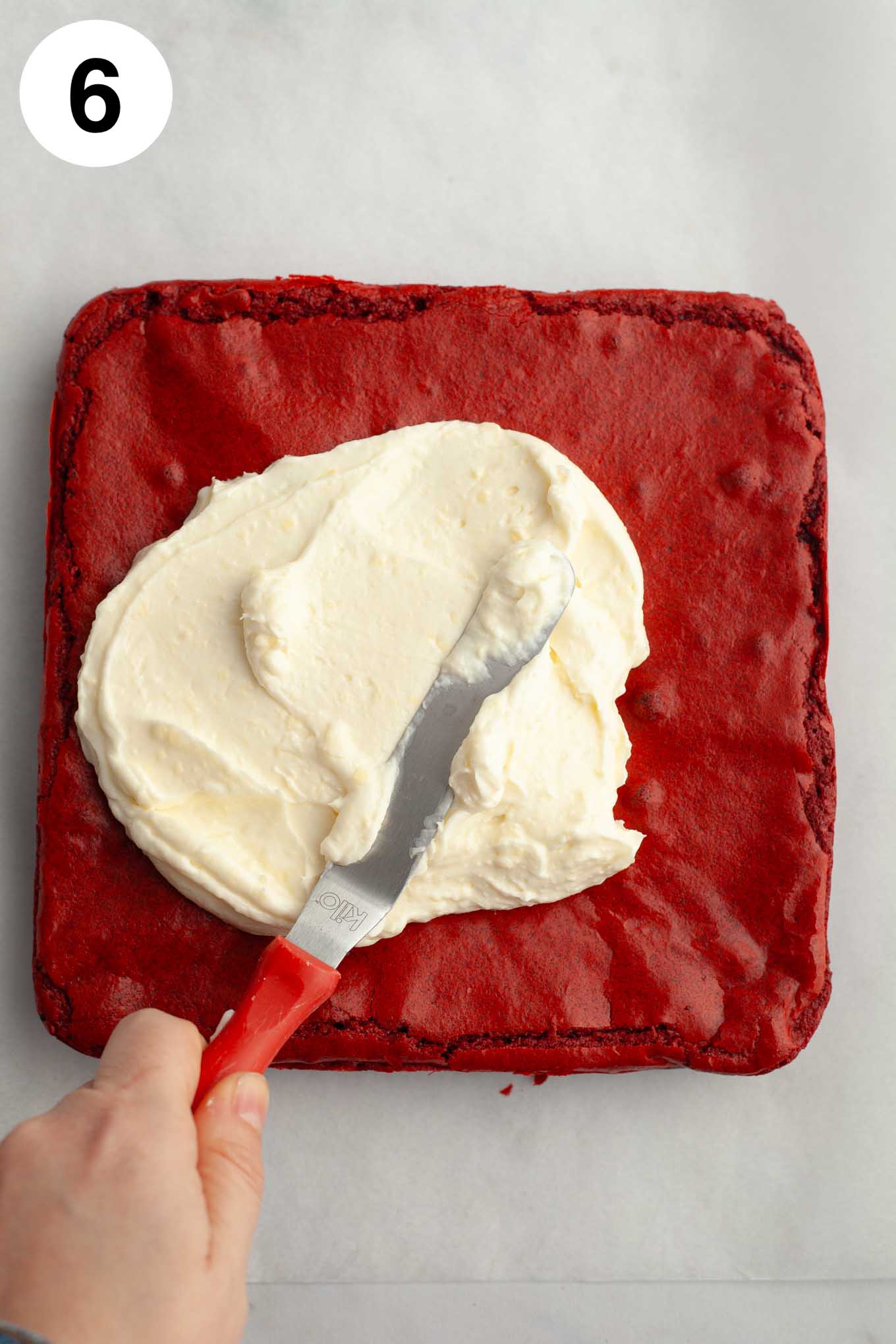 Una vista aérea del glaseado de queso crema que se extiende sobre los brownies con una espátula en ángulo.