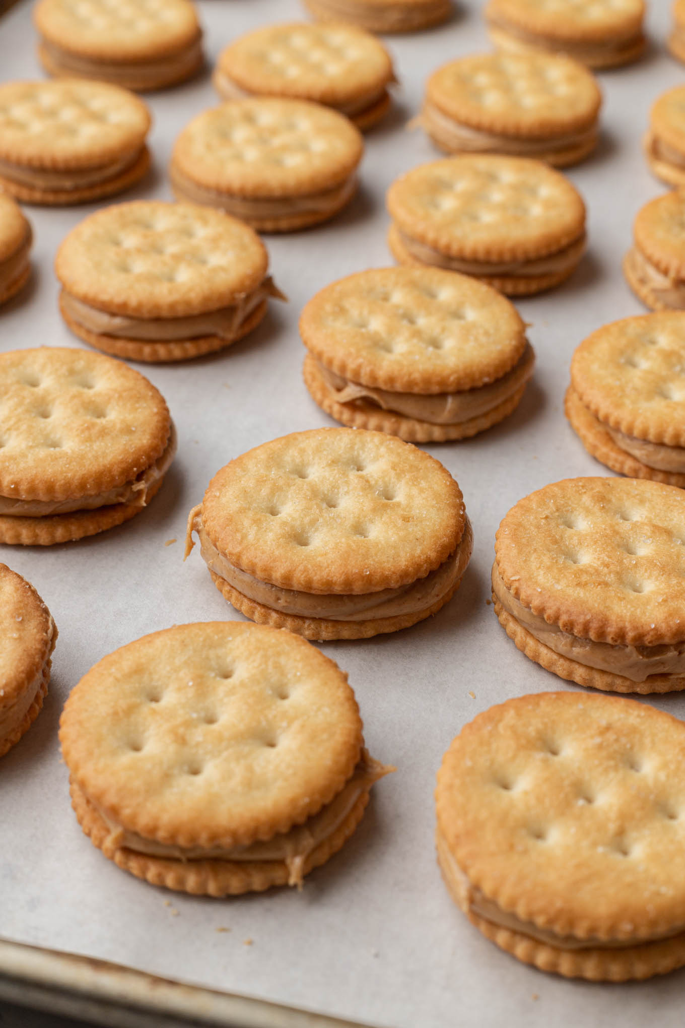 Filas de galletas saladas rellenas de mantequilla de maní, sobre una bandeja para hornear. 