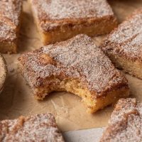 Una rubia snickerdoodle con un mordisco en un trozo de papel pergamino marrón.  Hay más rubias esparcidas a su alrededor.