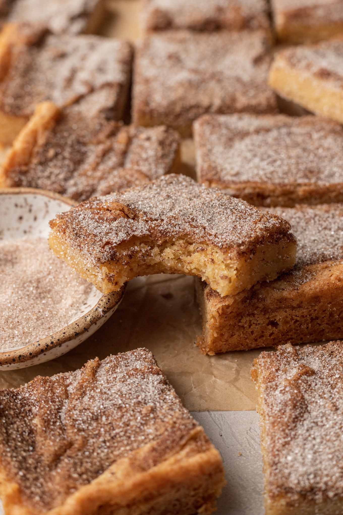 Barras de galletas Snickerdoodle sobre papel pergamino.  A una barra le falta un bocado y está apoyada encima de las demás. 