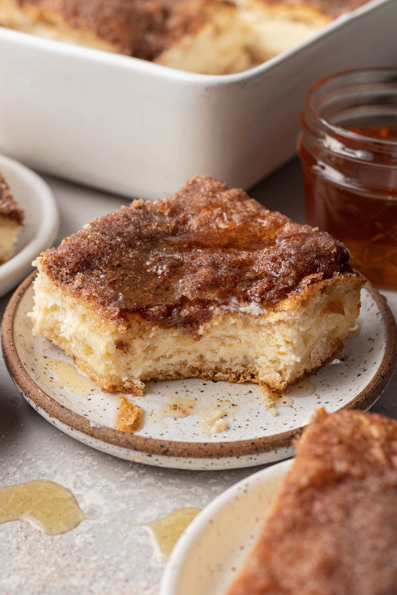 Una barra de tarta de queso y sopapilla en un plato de postre moteado, al que le falta un bocado. 