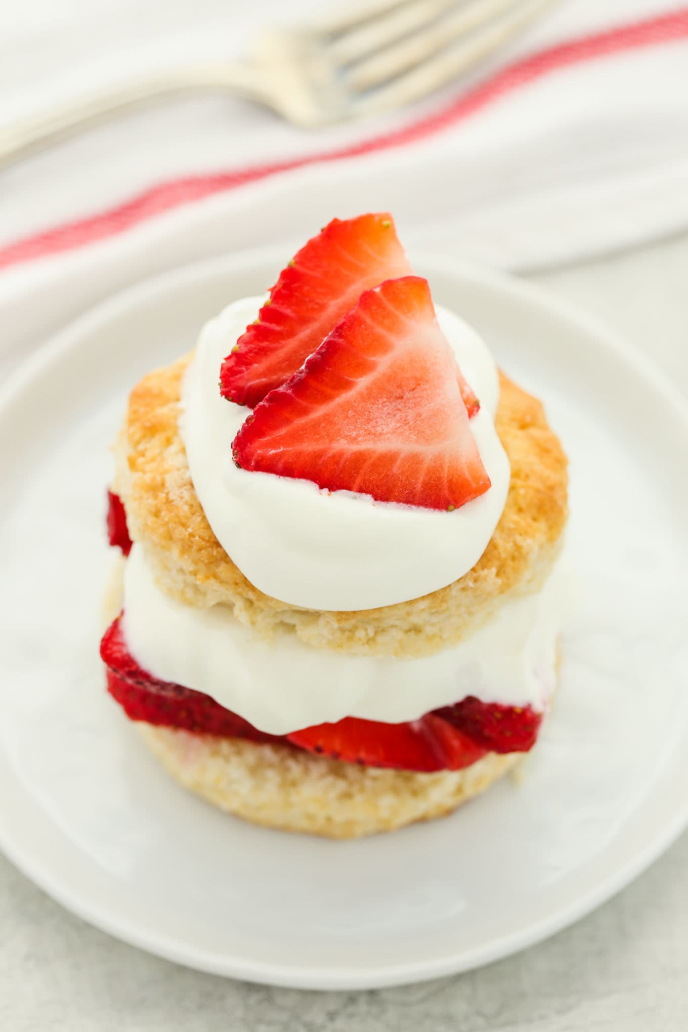 Tarta de fresas cubierta con crema batida extra y fresas en rodajas en un plato blanco.