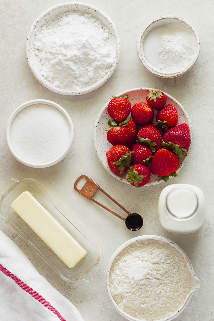 Varios de los ingredientes necesarios para la tarta de fresas sobre una superficie gris.