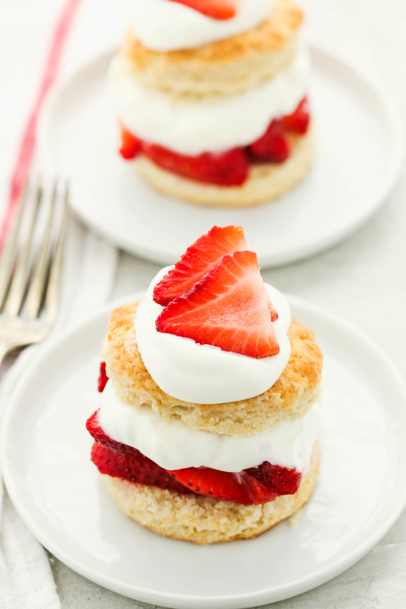 Dos tartas de fresa preparadas cubiertas con crema batida extra y fresas en rodajas en platos blancos.