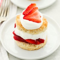 Tarta de fresas cubierta con crema batida extra y fresas en un plato blanco.